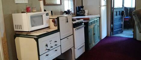 A compact kitchen with a microwave, stove, and refrigerator. There is a calendar on the wall and a window with blinds.