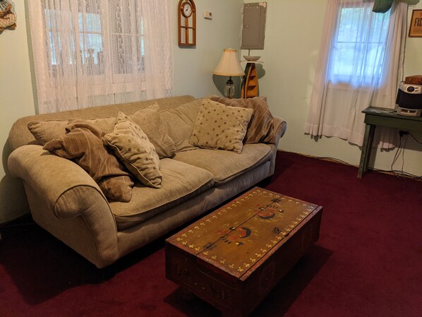 A living room with a sofa, a patterned coffee table, a lamp, and a clock on the wall.