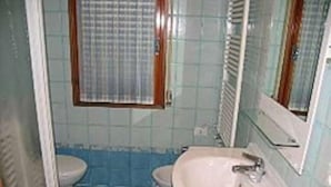 A bathroom with a toilet, sink, and window with blinds. - Mediterraneo (Lignano Sabbiadoro)