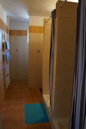 A shower area with a tiled floor, a blue mat, and a towel rack with towels. - Penzión 105 (Habovka)