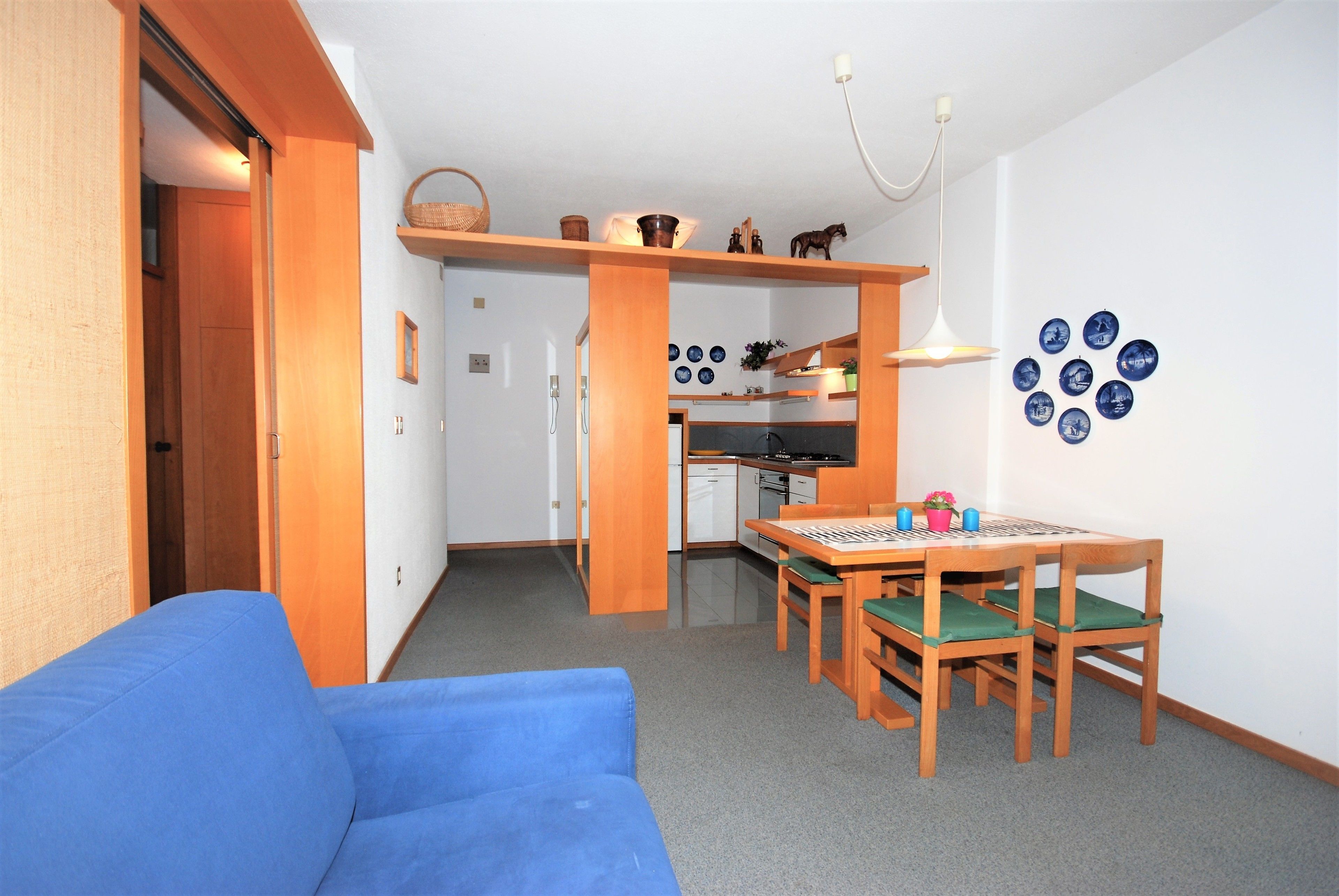 Un espace de vie compact comprenant un coin cuisine, un coin repas avec une table et des chaises, et un canapé bleu.