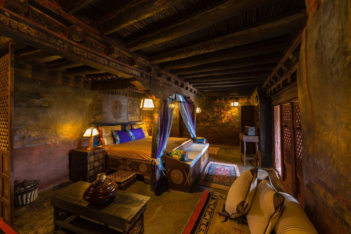 A traditional room with a four-poster bed, a wooden table, and a sofa.