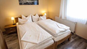 Una cama doble con ropa de cama blanca, dos mesitas de noche con lámparas, suelo de madera y un cuadro en la pared.