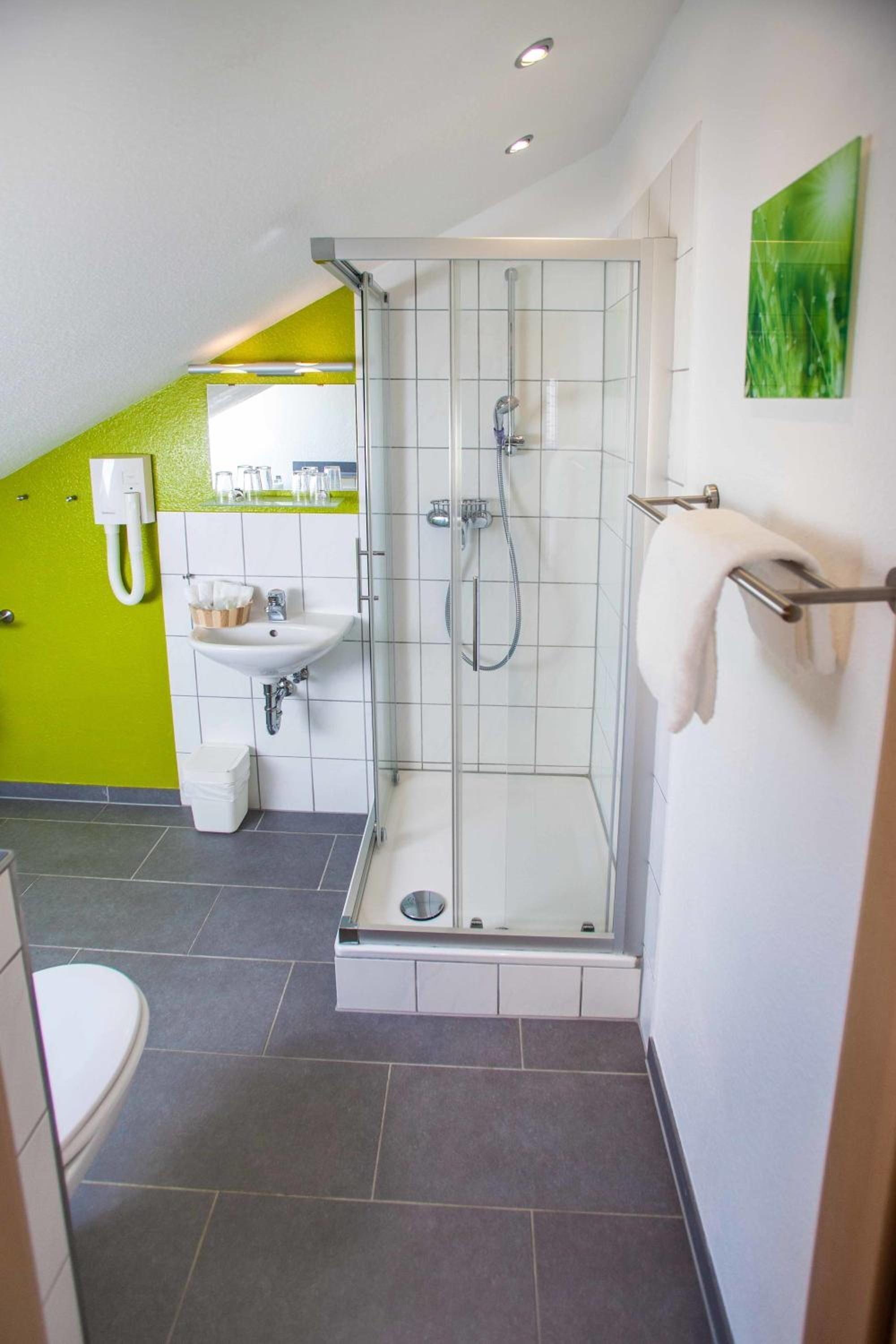 Un baño moderno con ducha envuelta en vidrio, lavamanos con espejo e inodoro.