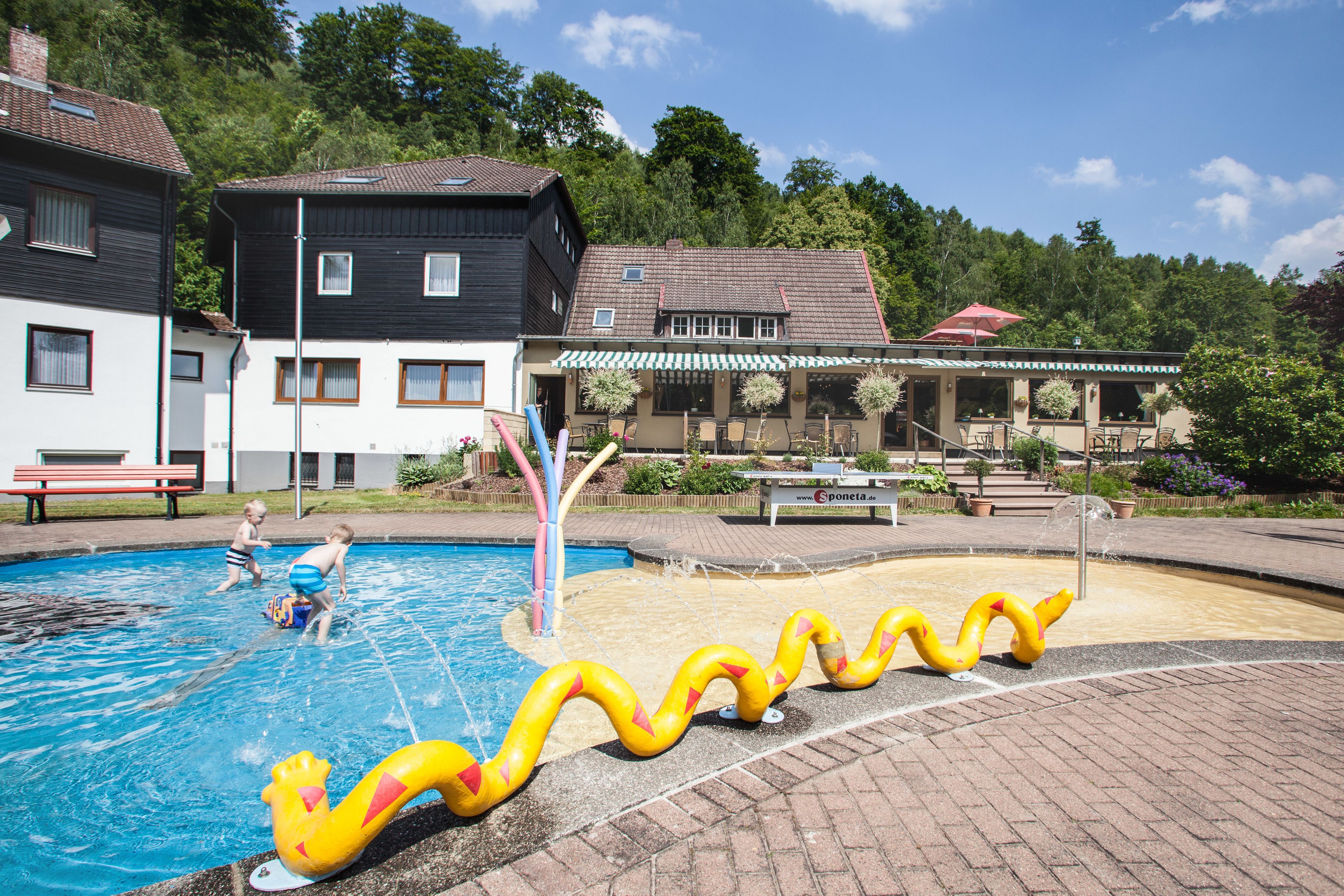 Una piscina con tobogán y dos niños jugando.