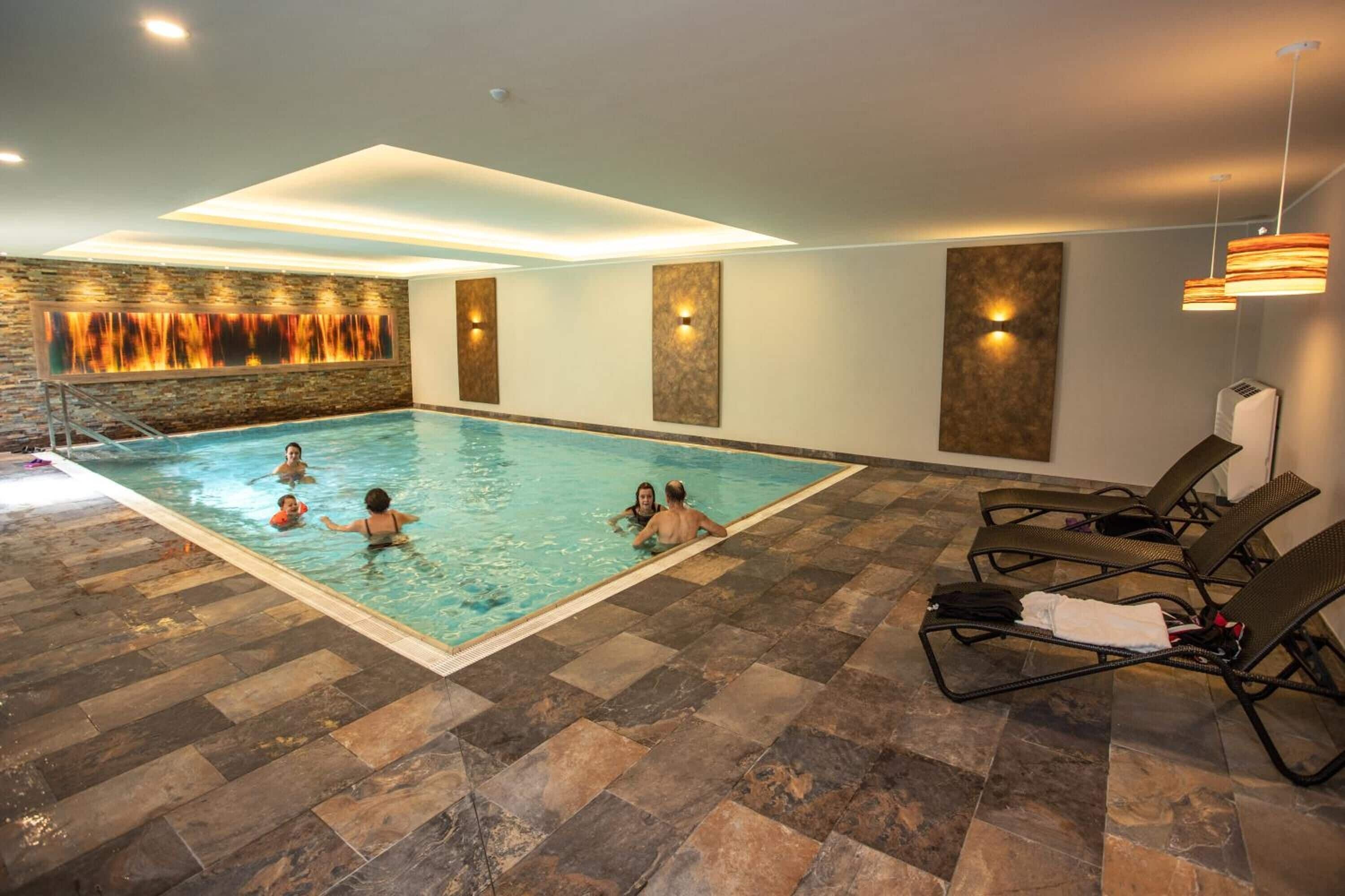 Una piscina interior con suelo de baldosas, sillas de descanso e iluminación empotrada.
