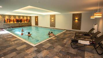 Una piscina interior con suelo de baldosas, sillas de descanso e iluminación empotrada.