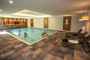 An indoor swimming pool with tiled flooring, lounge chairs, and wall-mounted lights. - Hotel Im Tannengrund (Langelsheim)