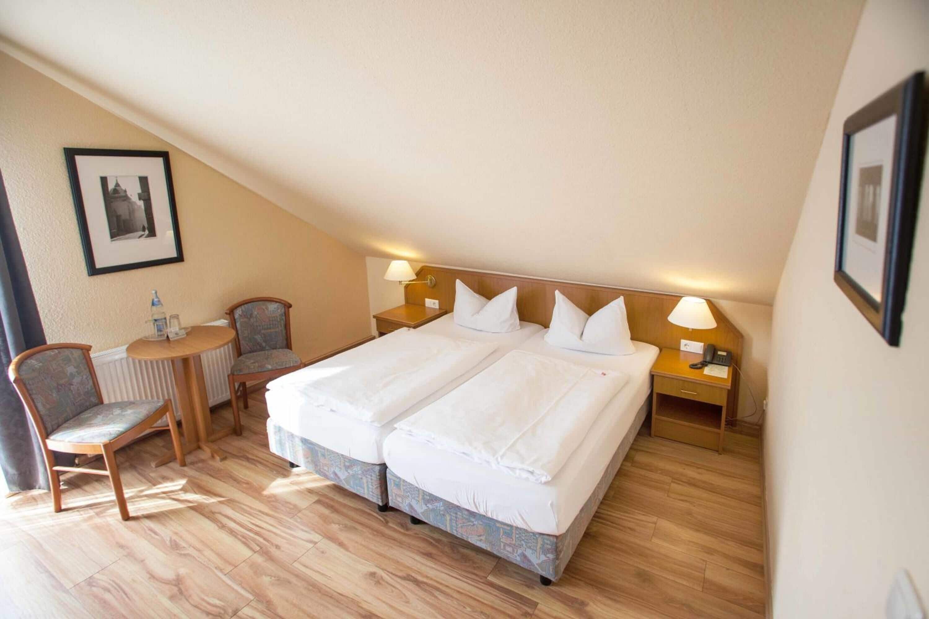 Une chambre d’hôtel avec un grand lit, deux tables de chevet, une chaise et une petite table avec une lampe.