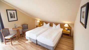 Een hotelkamer met een groot bed, twee nachtkastjes, een stoel en een klein tafeltje met een lamp.