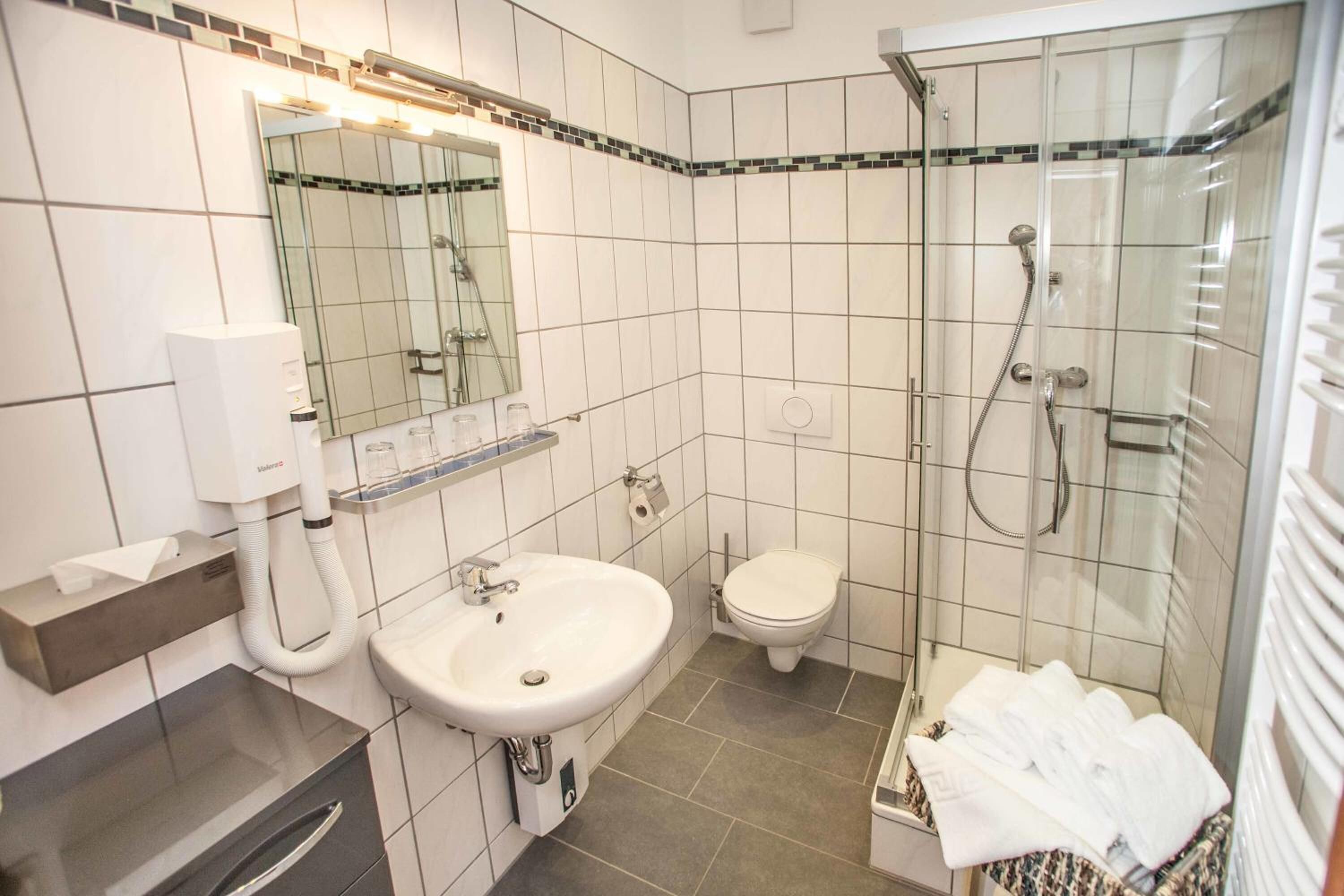 Baño con lavamanos, inodoro y ducha con mampara de vidrio.