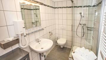 Baño con lavamanos, inodoro y ducha con mampara de vidrio.