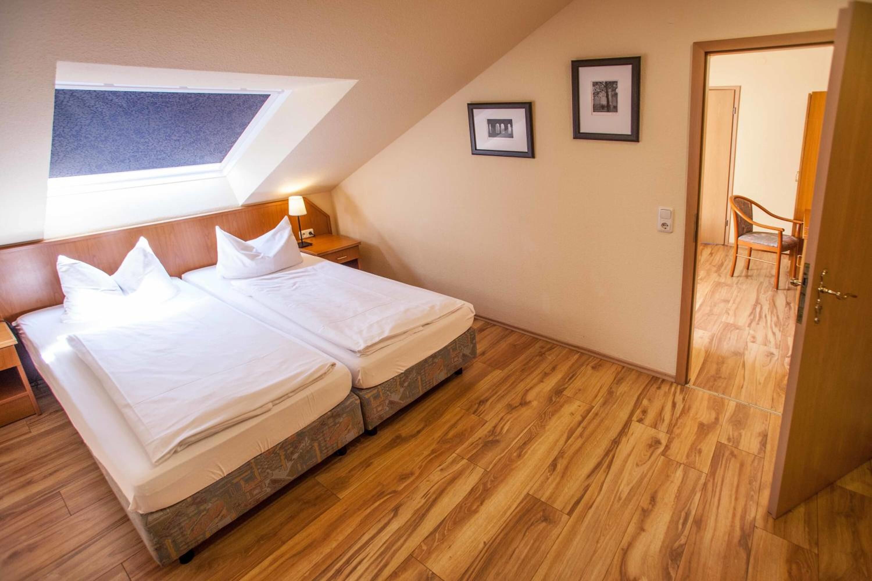 Un dormitorio con dos camas, un tragaluz, suelo de madera y una puerta que da a otra habitación.