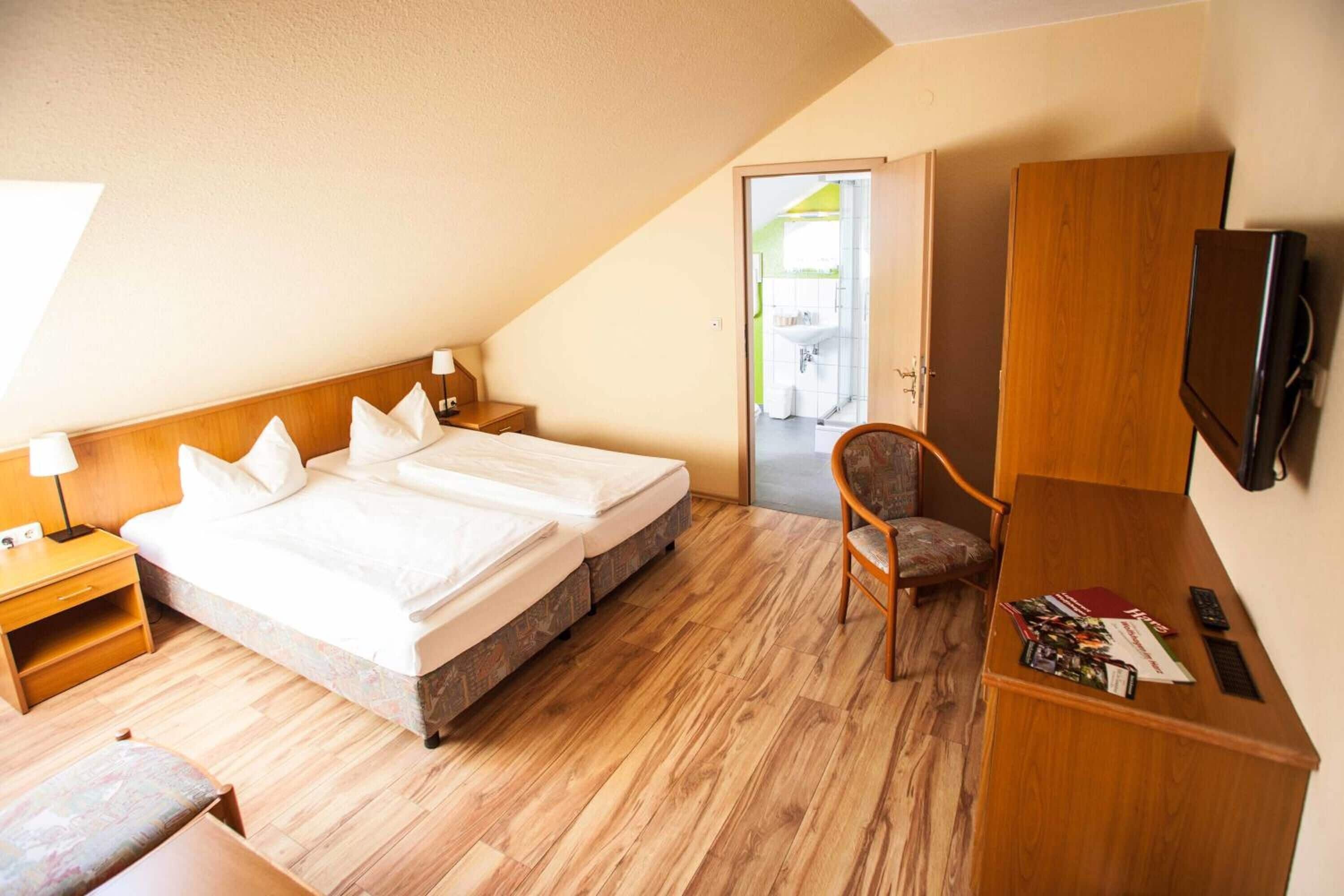 A hotel room with a large bed, a desk with a chair, a television, and a wardrobe.
