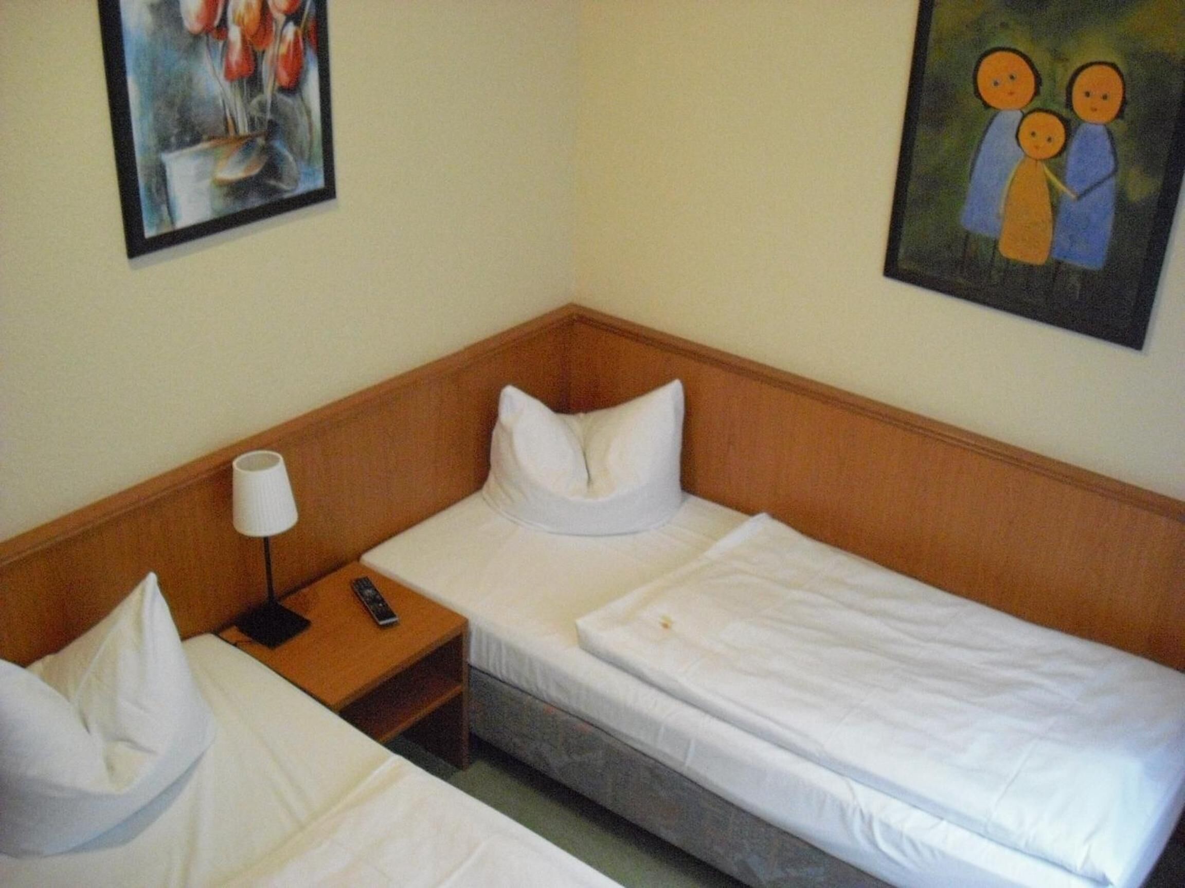 Una habitación de hotel pequeña con dos camas individuales, una mesita de noche con una lámpara y un cuadro en la pared.