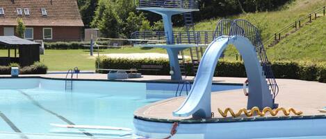 A swimming pool with a slide, a diving platform, and a staircase leading to a hill.
