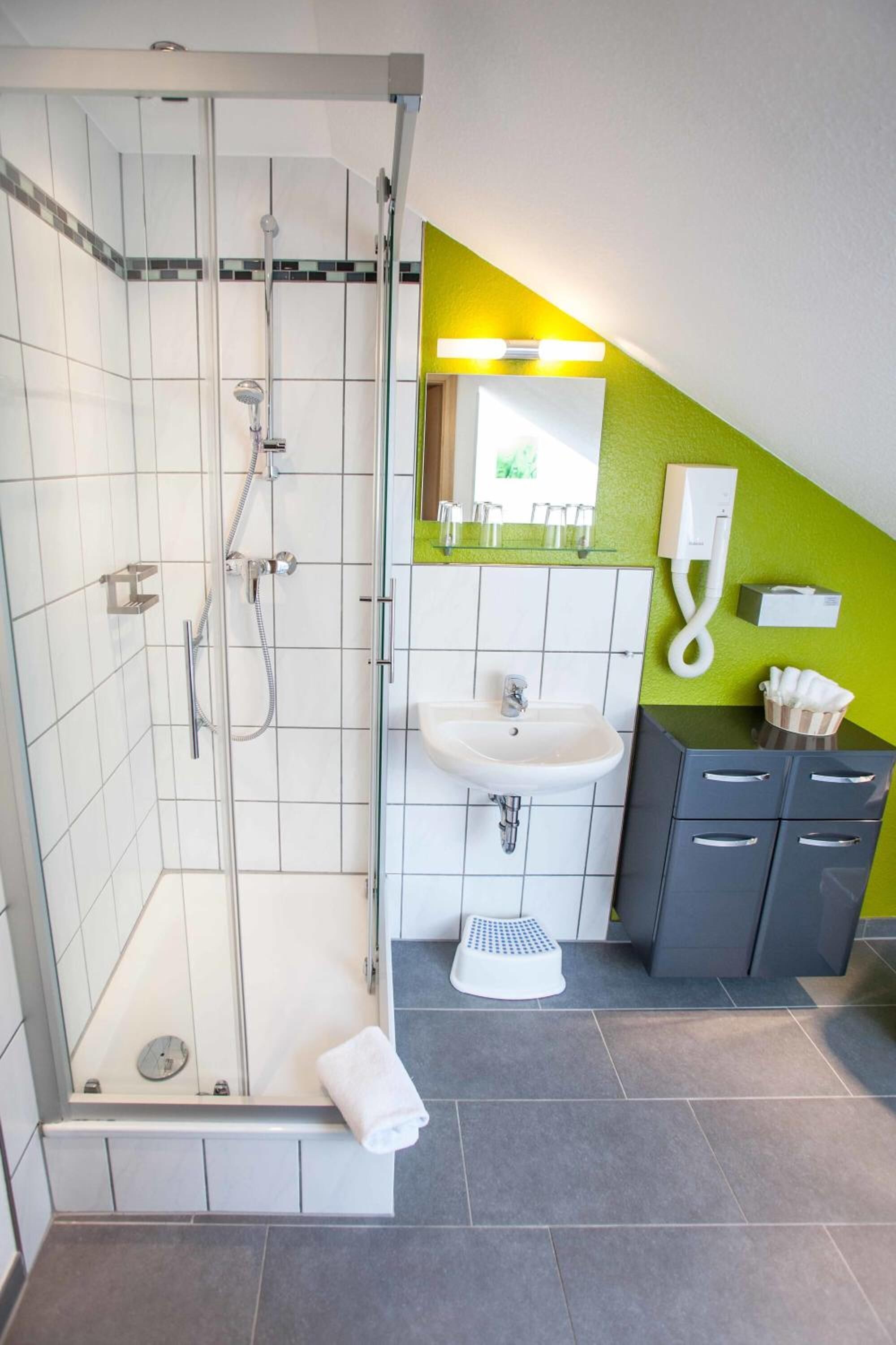 Un baño moderno con ducha de vidrio, lavamanos y tocador con cajones.