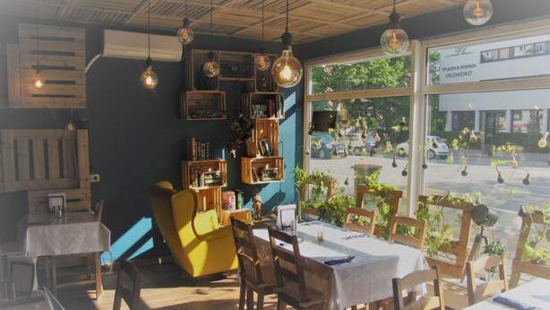 A cozy restaurant interior with wooden furniture, hanging light bulbs, and a view of the street outside. - Milano Hotel (Hamburg)