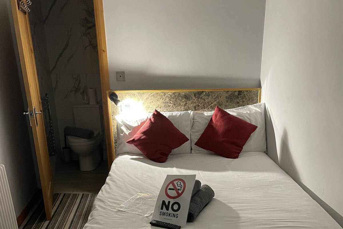 Ein Hotelzimmer mit einem Bett, einem Rauchverbot-Schild, einer Fernbedienung und einem durch eine offene Tür einsehbaren Badezimmer.
