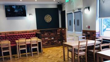 A restaurant with a herringbone wooden floor, red leather booth seating, and a dartboard on the wall.