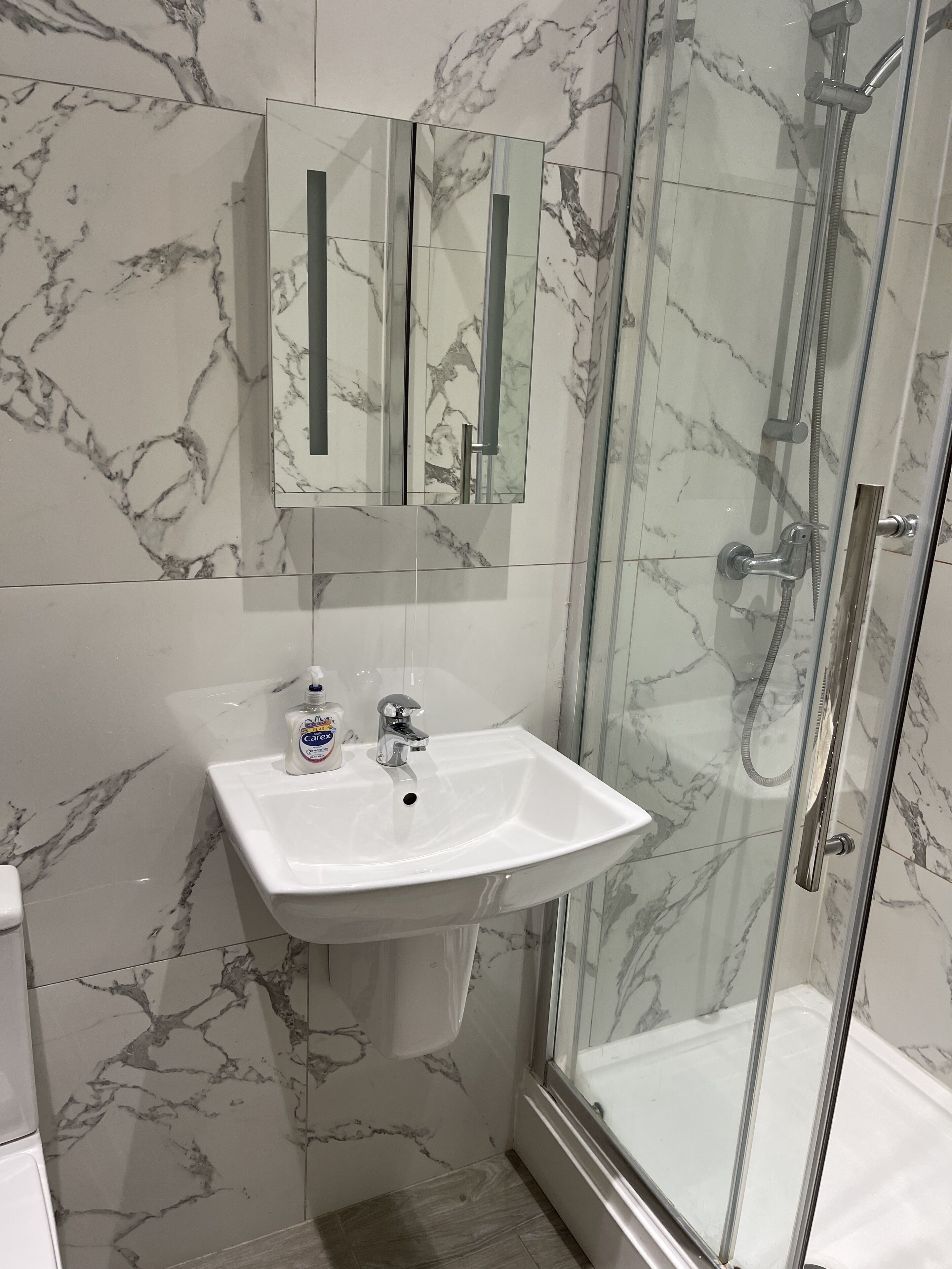 A bathroom with a marble backsplash, a white sink, a mirror, and a glass-enclosed shower.