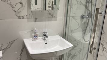 A bathroom with a marble backsplash, a white sink, a mirror, and a glass-enclosed shower.