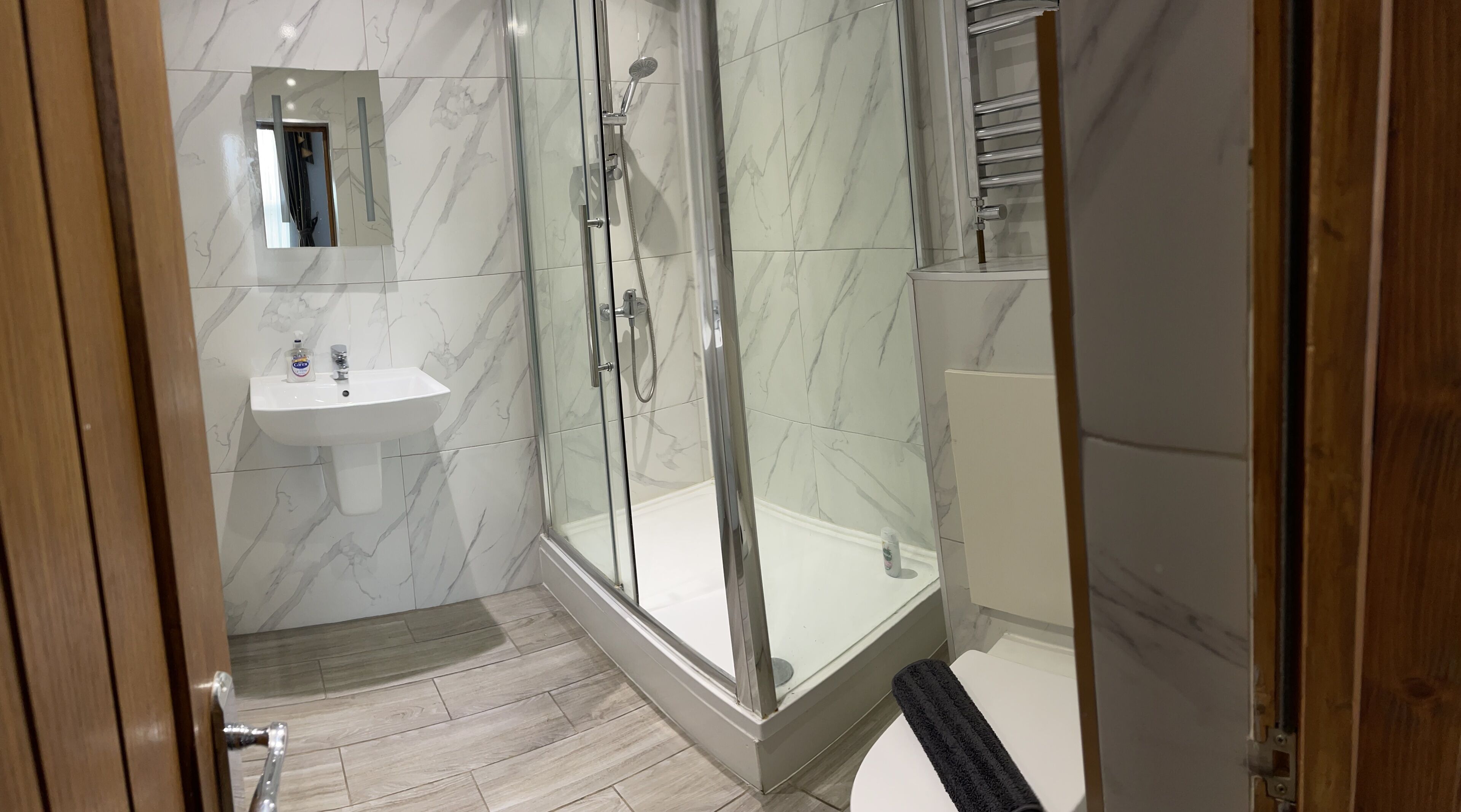 A modern bathroom with a glass-enclosed shower, a white sink, and a marble-tiled wall.