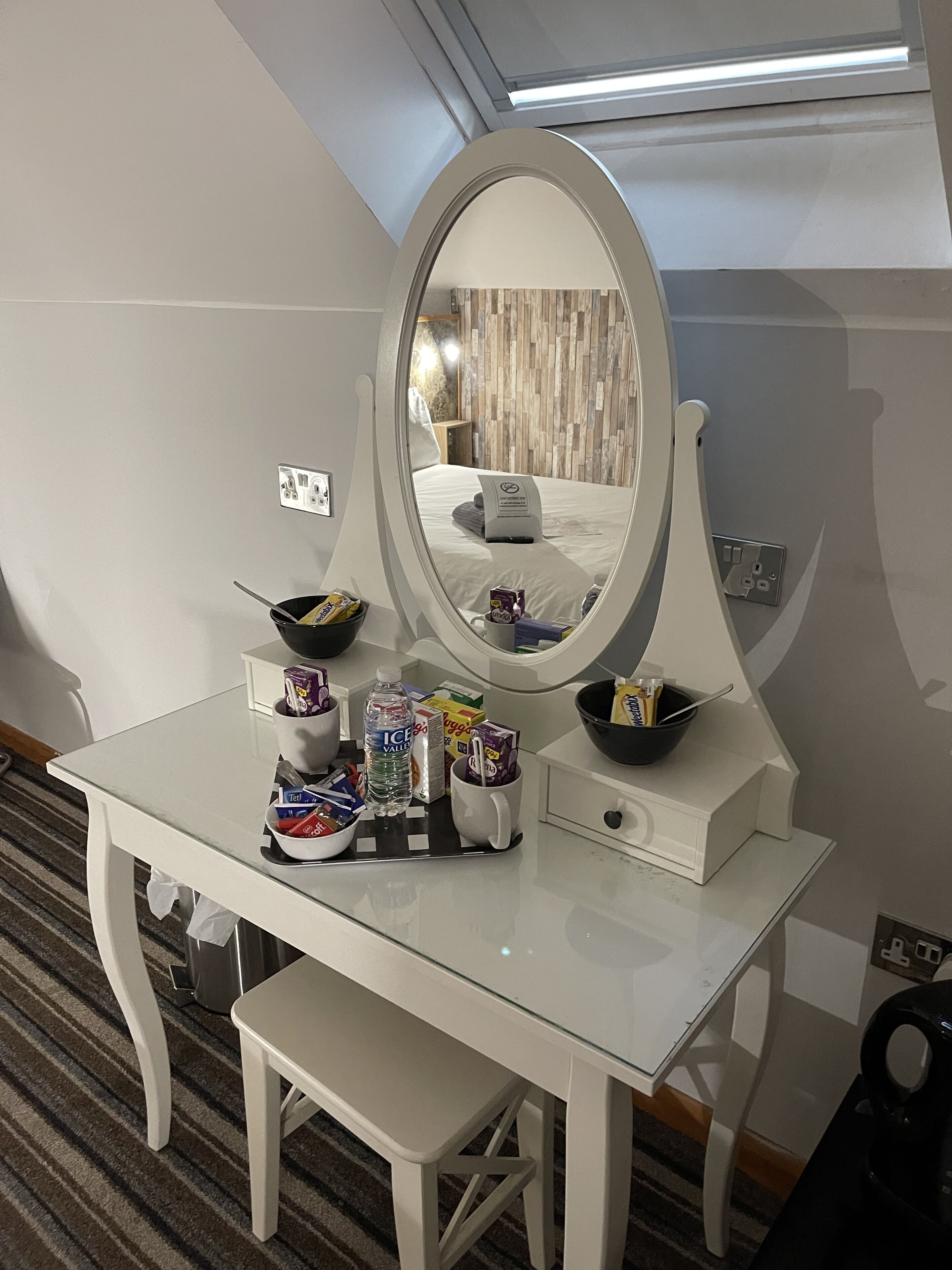 A white vanity with a large mirror, a bowl, and various toiletries.