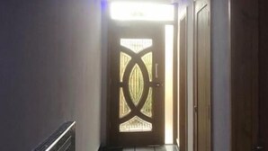 A hallway with a decorative door at the end, a ceiling with recessed lighting, and a tiled floor. - Six Bells Hotels (Enfield)