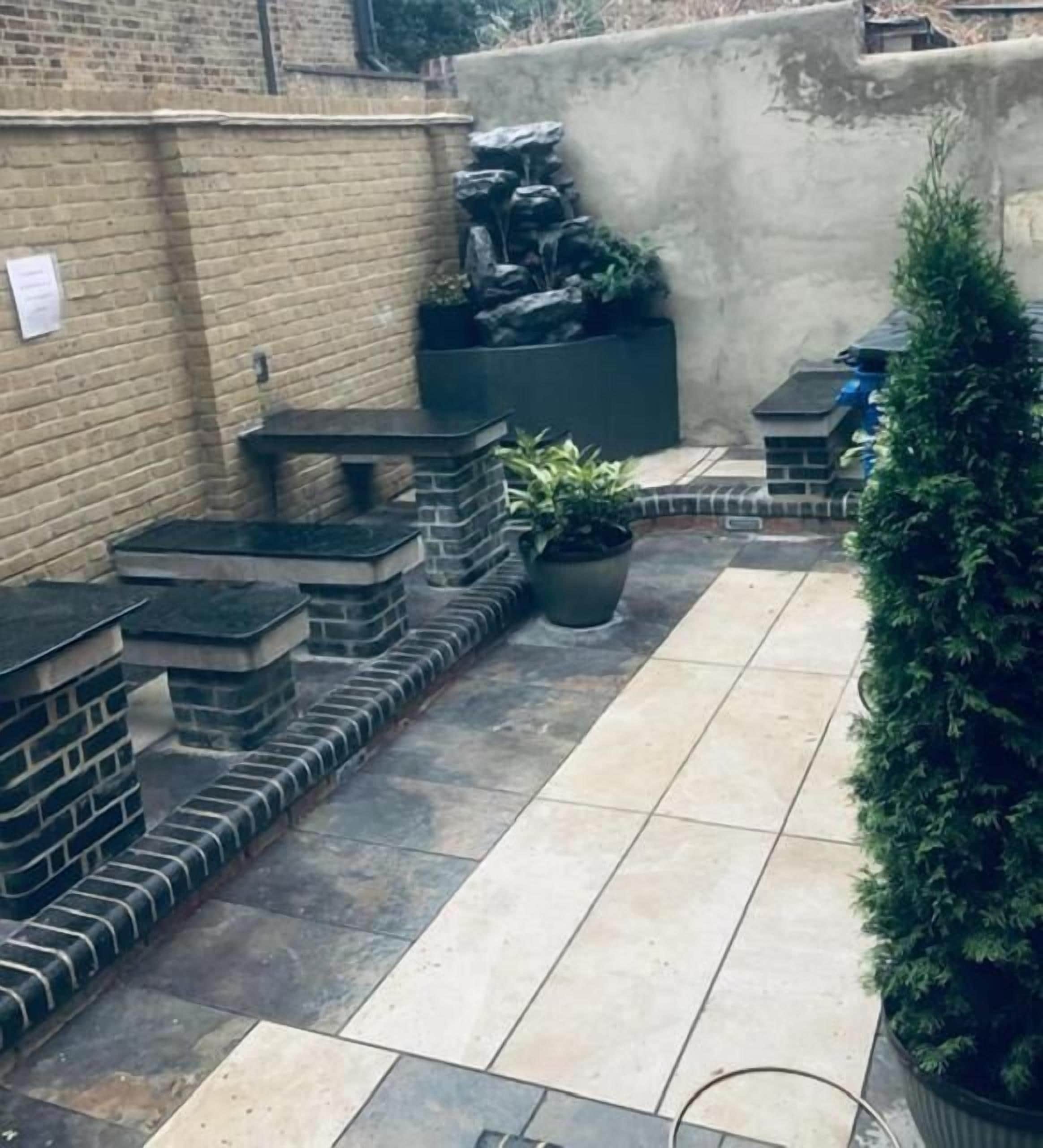 A patio area with stone steps leading to a seating area, a potted plant, and a small waterfall feature.