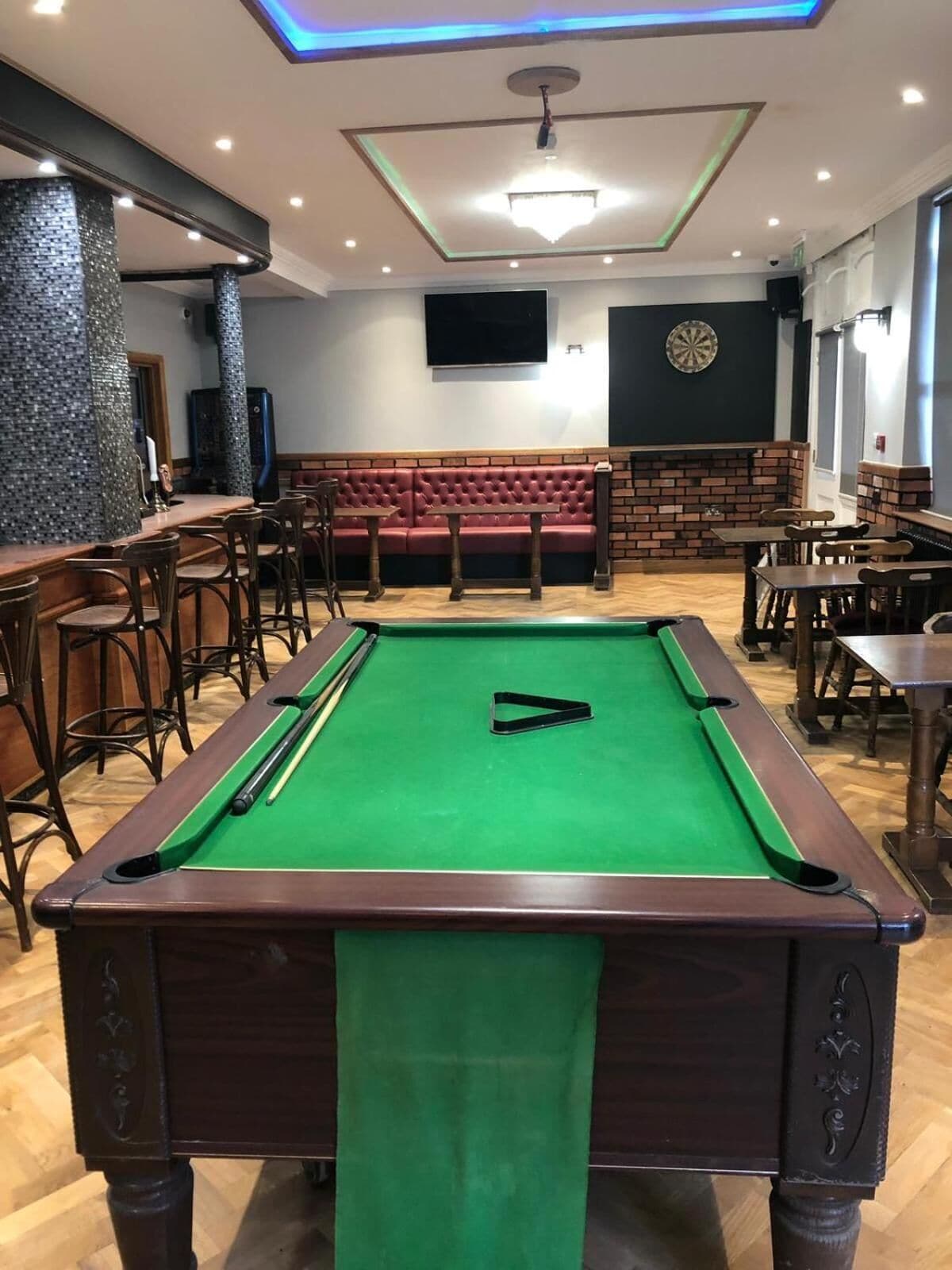 A billiards table with a green felt surface, surrounded by wooden chairs and tables.