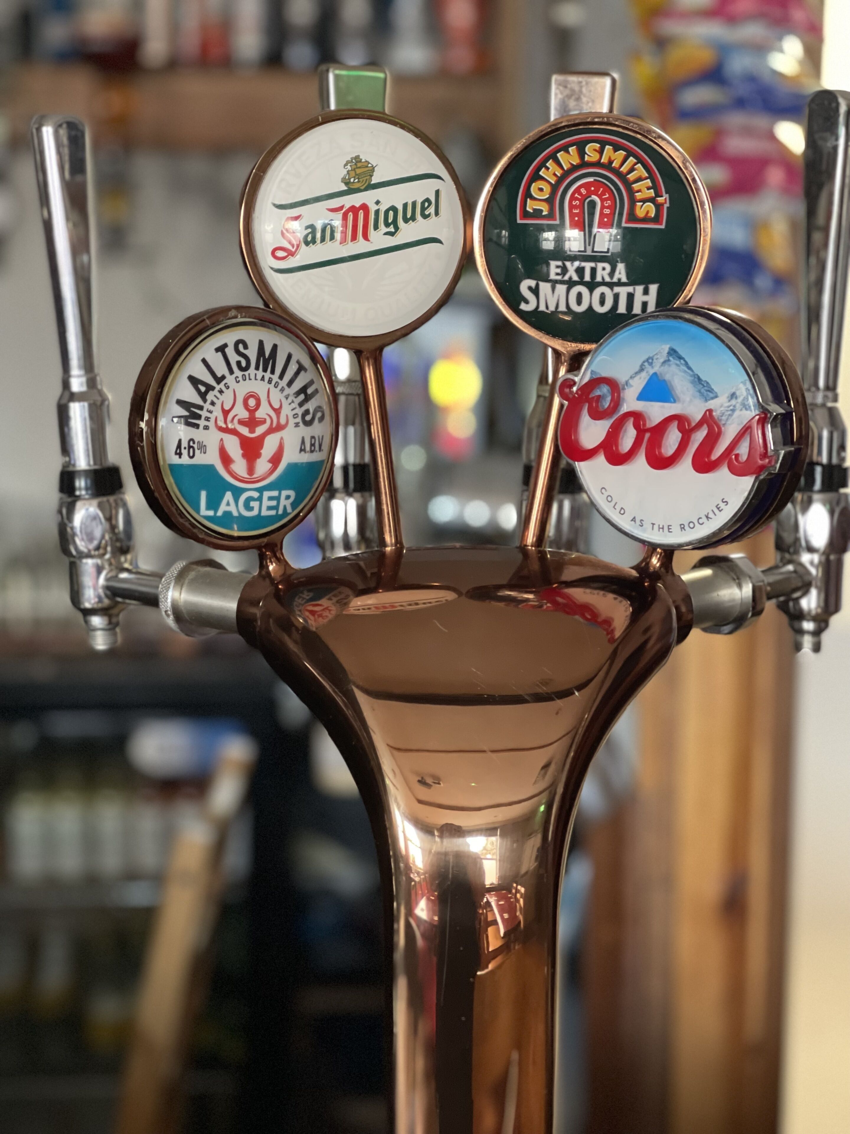 A beer tap with labels for San Miguel, John Smith's, Coors, and Malt Smiths.