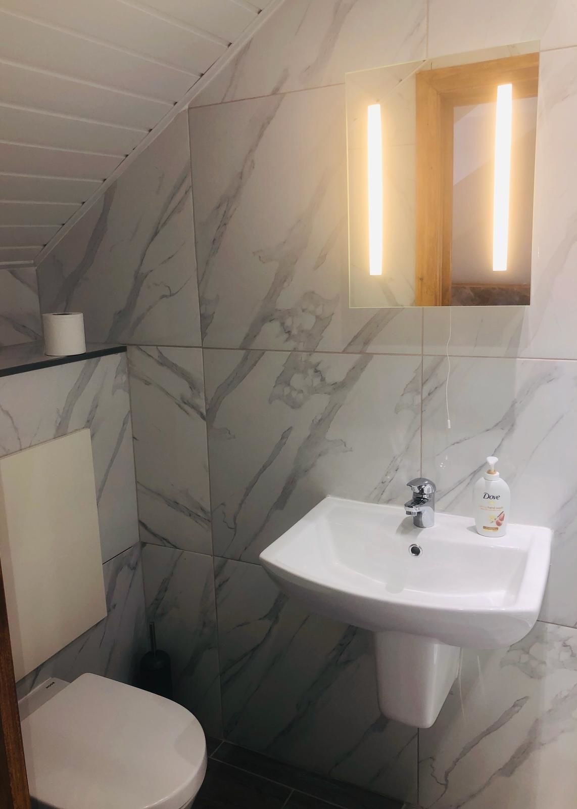 A bathroom with a marble wall, a white sink with a Dove soap dispenser, and a toilet.