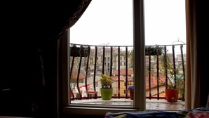 Ein Balkon mit Blick auf eine Stadtlandschaft, mit einem Fenster, einem Metallgeländer und Kübelpflanzen.
