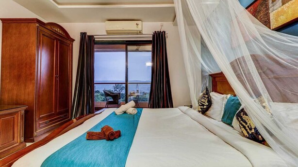 A bedroom with a large bed, a view of the sea, and a wooden wardrobe. - Mahinder Inn By Sapphire Stays (Mahabaleshwar)