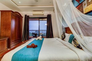 A bedroom with a large bed, a view of the sea, and a wooden wardrobe.