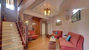 A spacious living area with a staircase, red sofas, a coffee table, and a chandelier. - Mahinder Inn By Sapphire Stays (Mahabaleshwar)