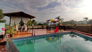 A pool area with a wooden deck, lounge chairs, and a covered seating area. - Mahinder Inn By Sapphire Stays (Mahabaleshwar)