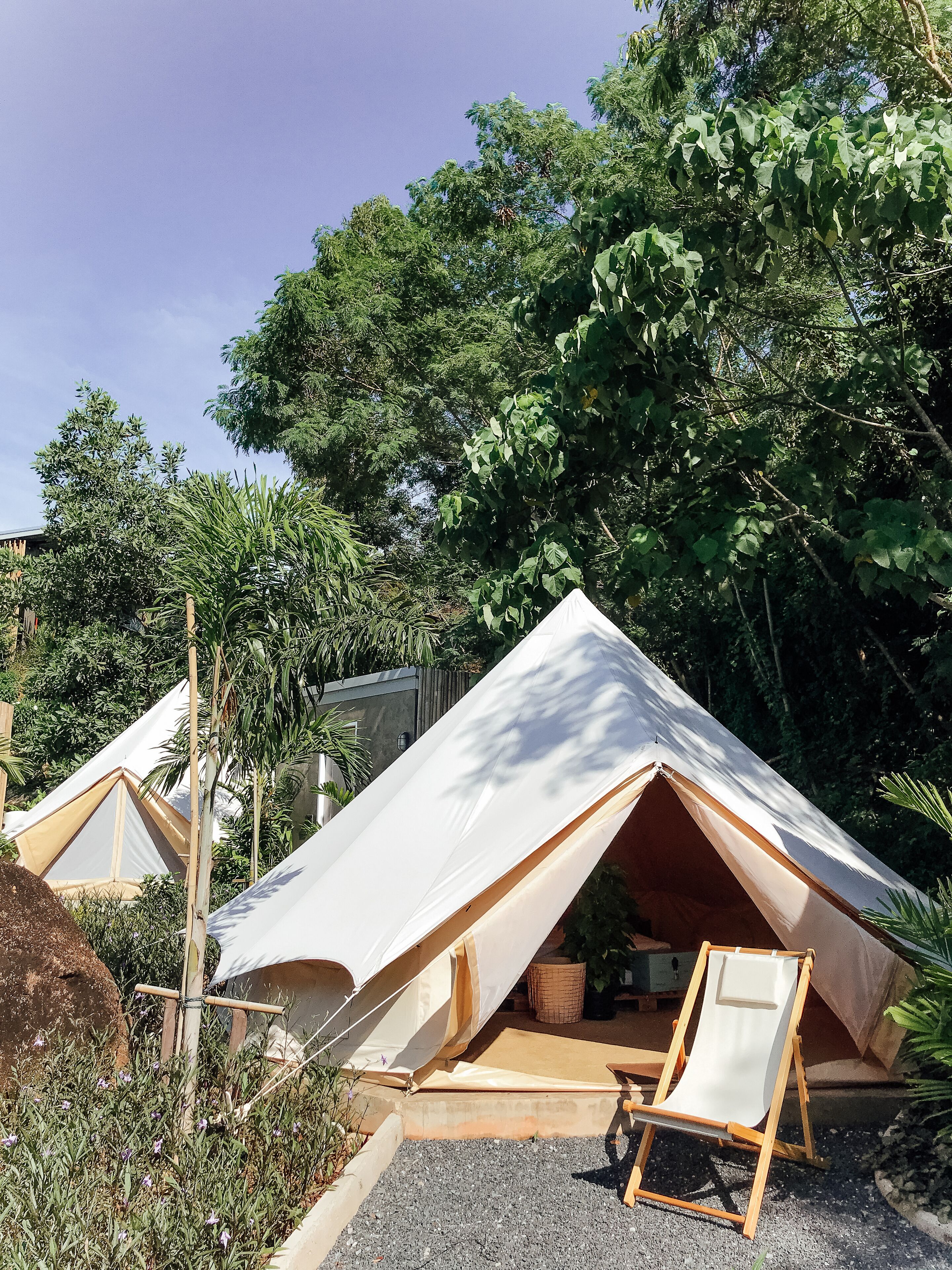 A tented accommodation with a wooden deck and a beach chair, surrounded by dense foliage.