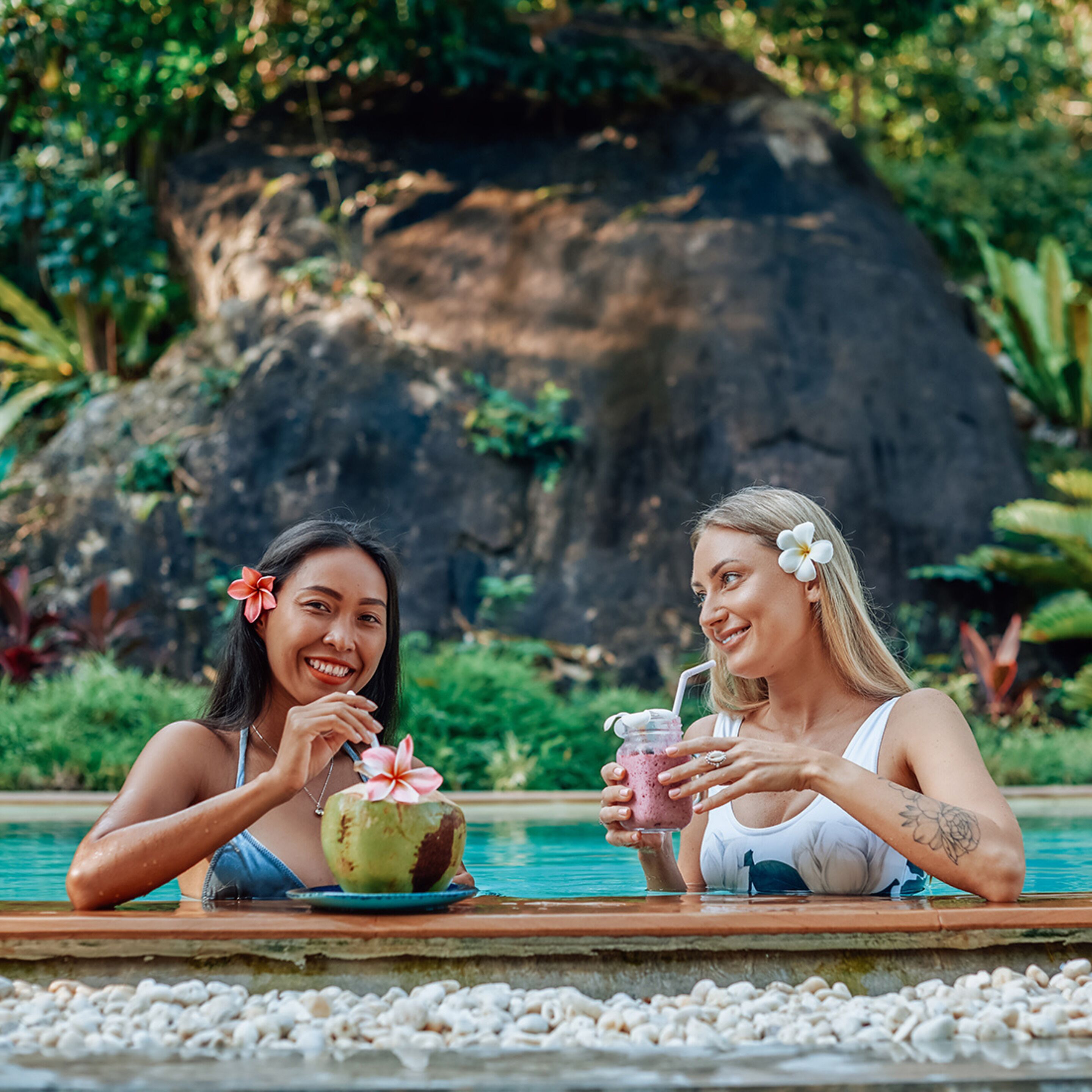 Two people sitting by a pool with drinks and a coconut.