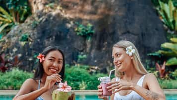 Two people sitting by a pool with drinks and a coconut.