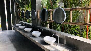 A row of white sinks with modern faucets, set against a backdrop of lush greenery and a concrete structure.