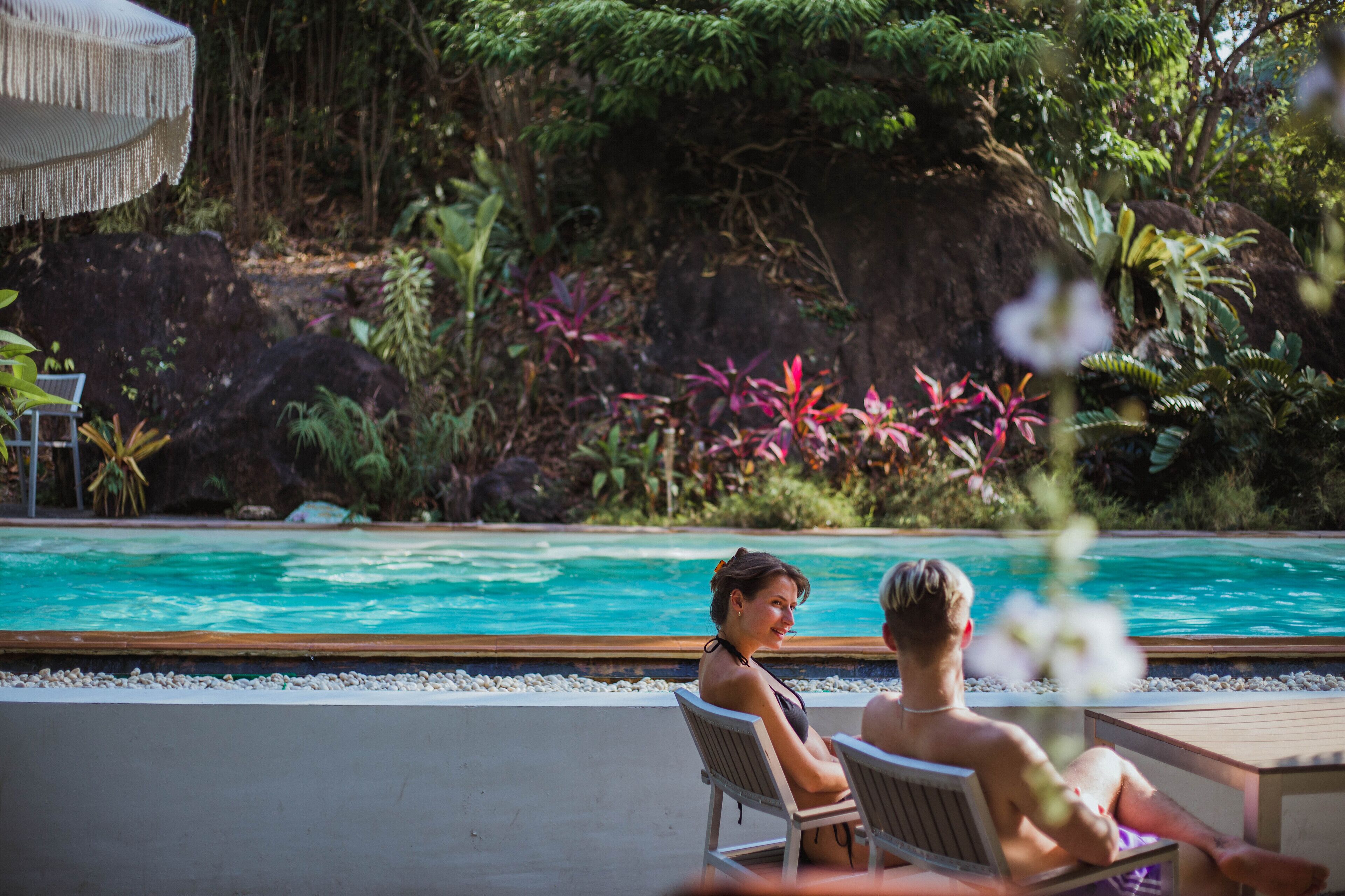 A poolside area with two lounge chairs, a wooden deck, and a natural backdrop of rocks and vegetation.