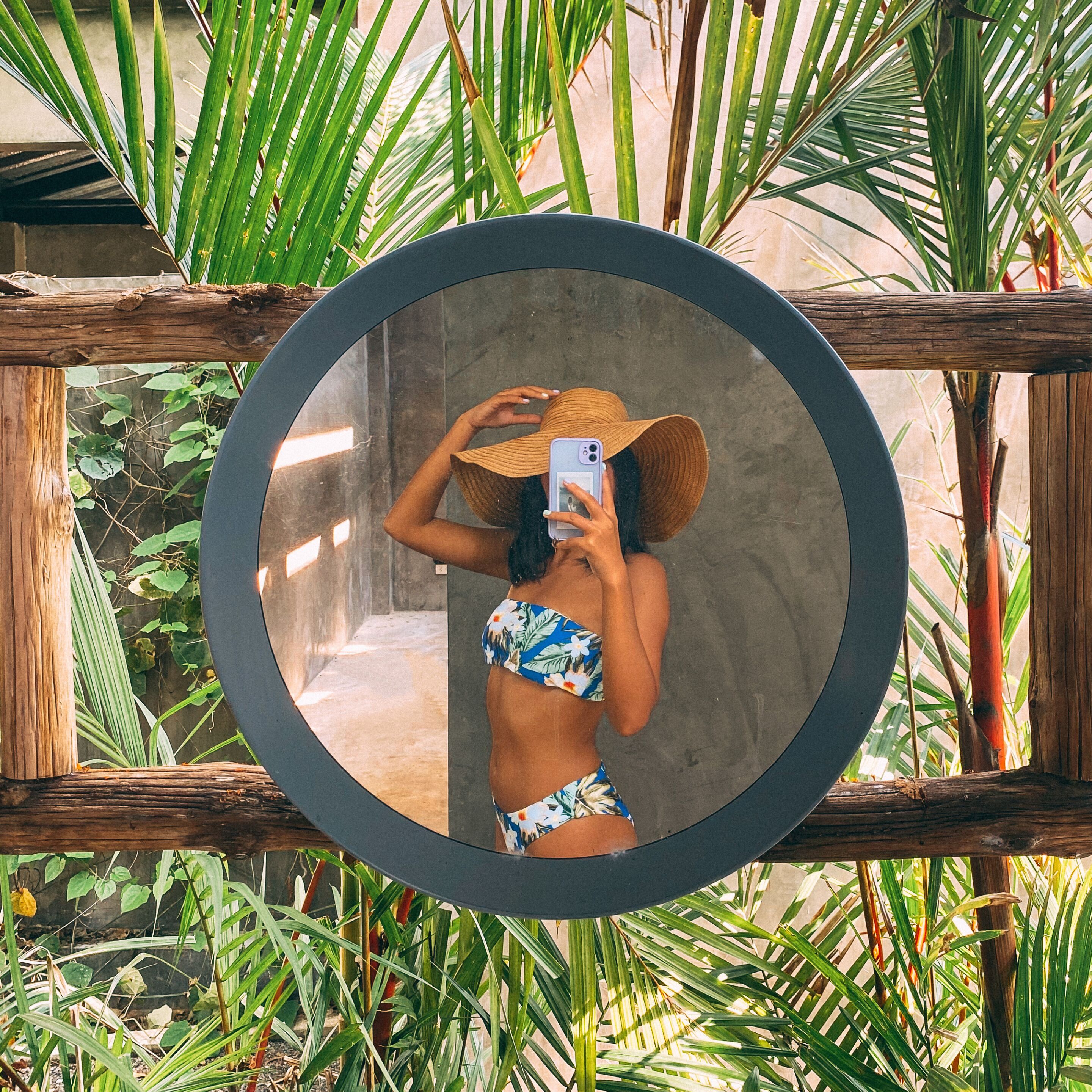 Una persona tomándose un selfie frente a un espejo con un paisaje tropical.