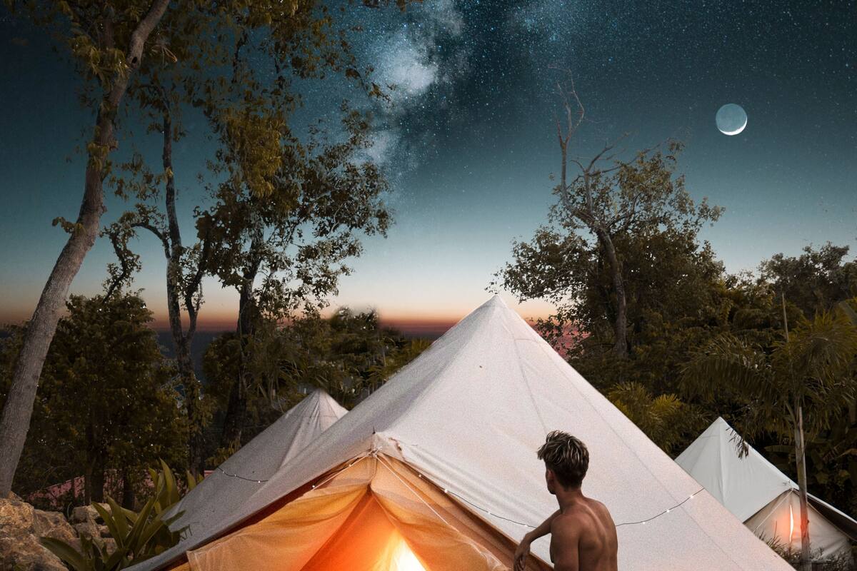 A tent with a lit interior, surrounded by trees and a night sky with stars and a moon.