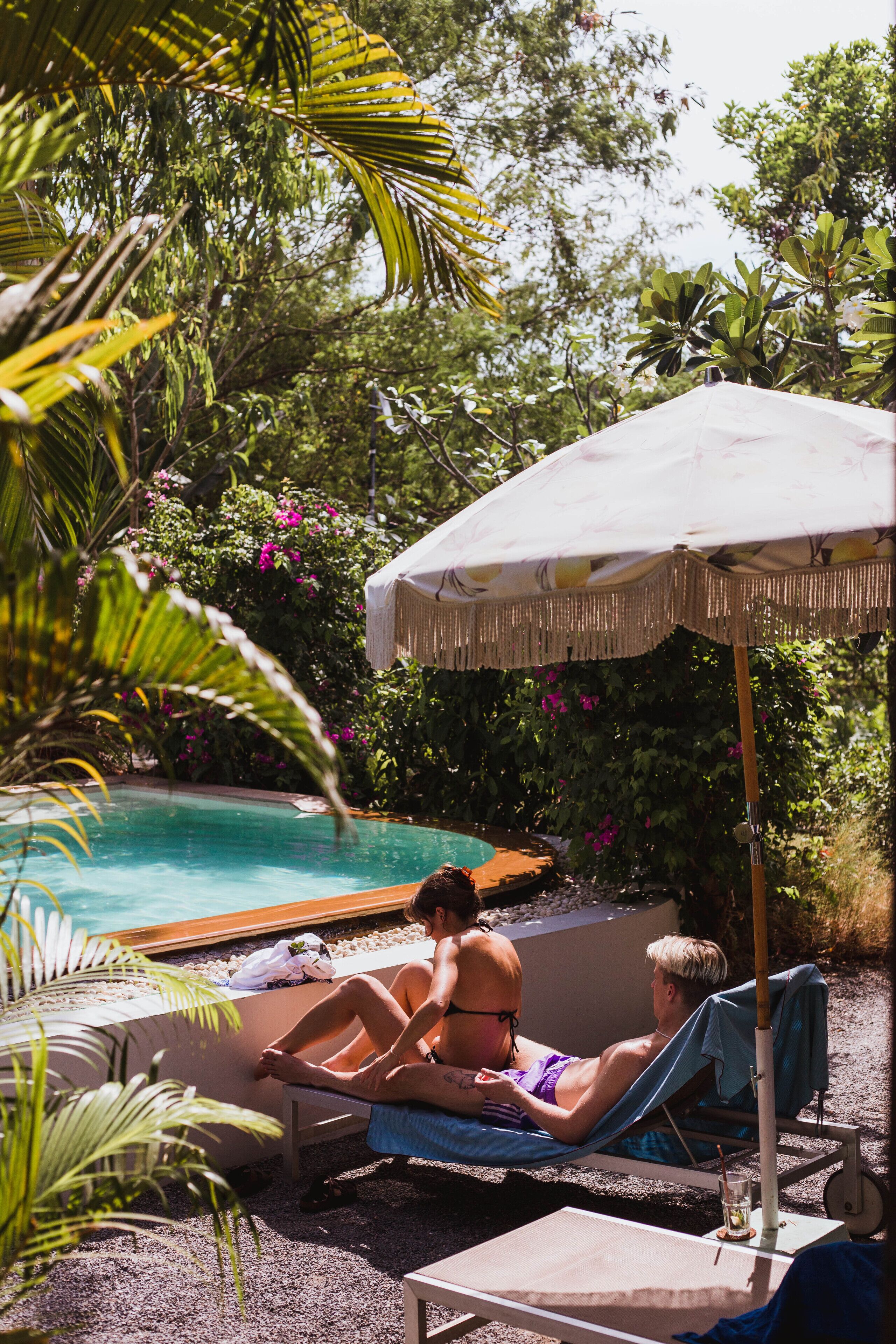 A poolside area with lounge chairs, an umbrella, and a pool.