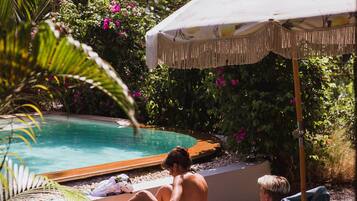 A poolside area with lounge chairs, an umbrella, and a pool.