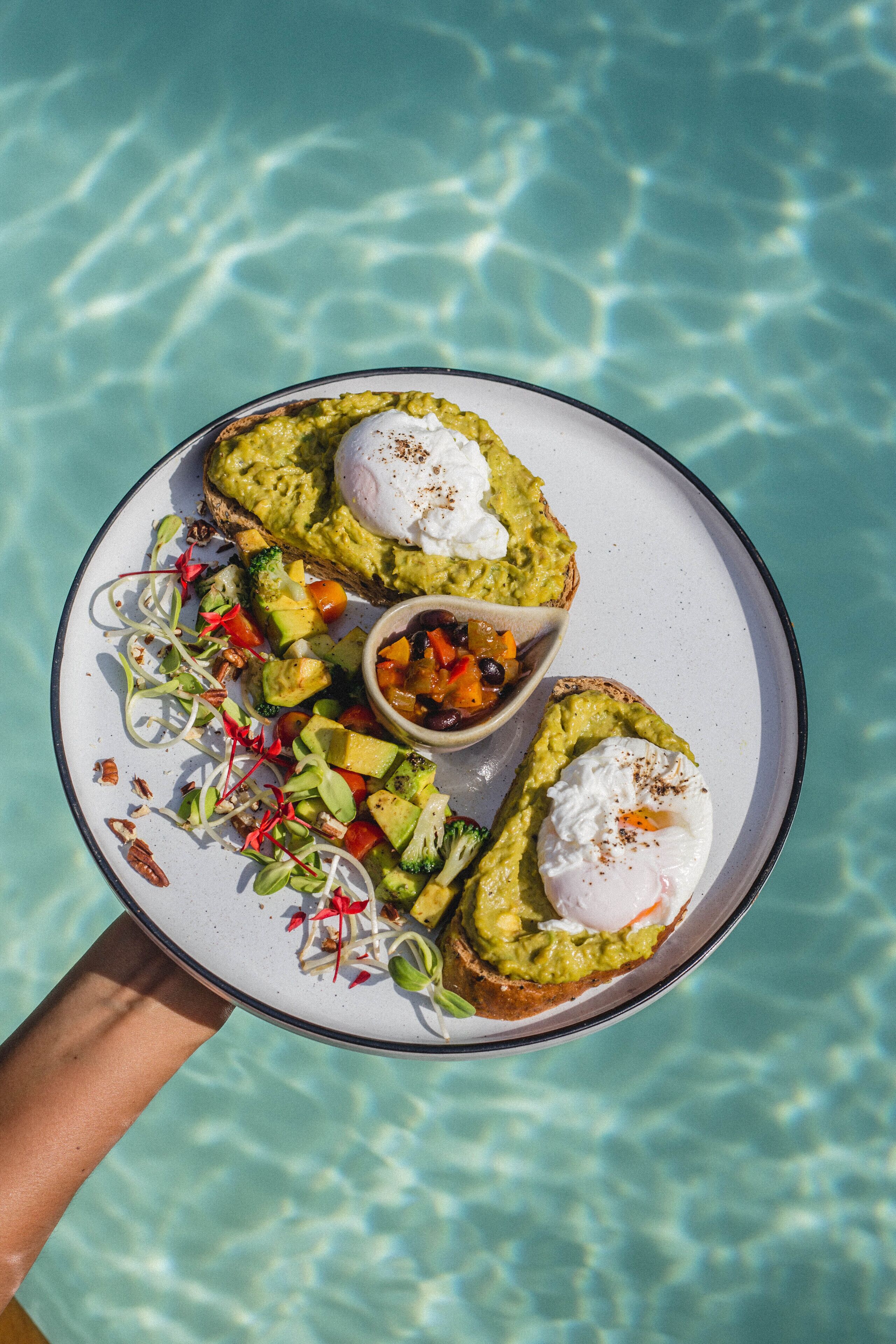 A plate with avocado toast and a side salad, held over a pool.