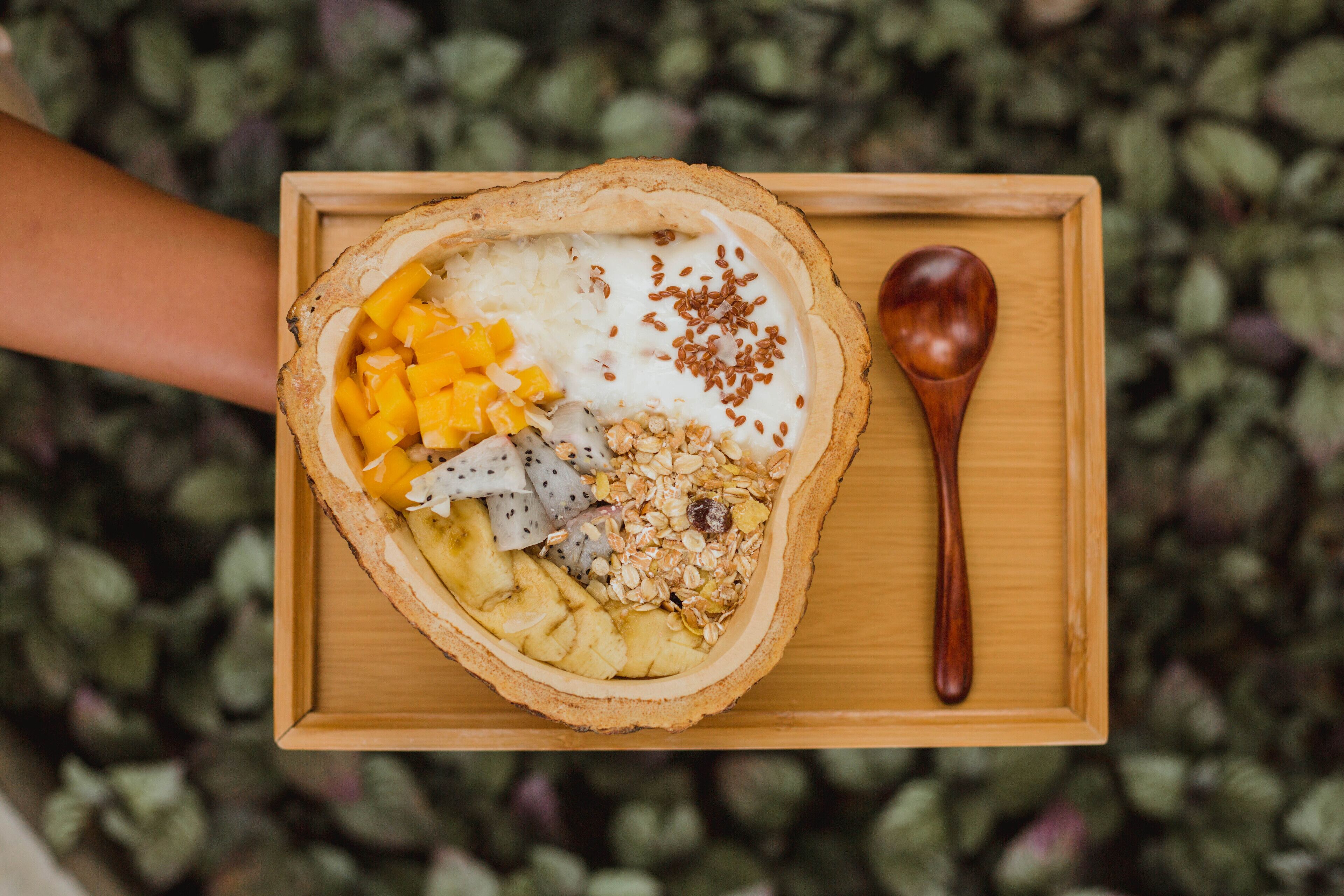 A wooden tray with a bowl of fruit and yogurt, accompanied by a wooden spoon.