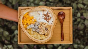 A wooden tray with a bowl of fruit and yogurt, accompanied by a wooden spoon.